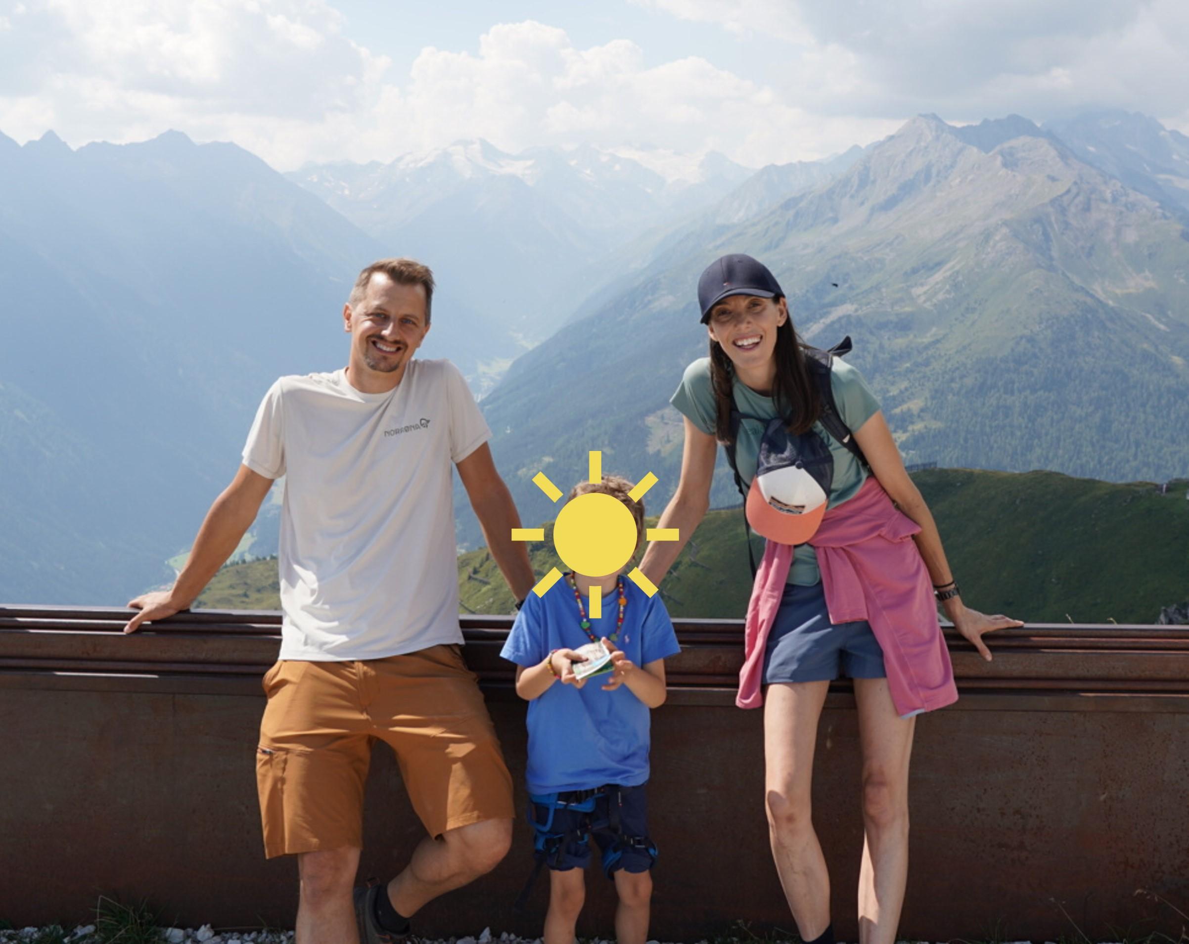 A family of father, mother and son are smiling and posing in front of a mountain range